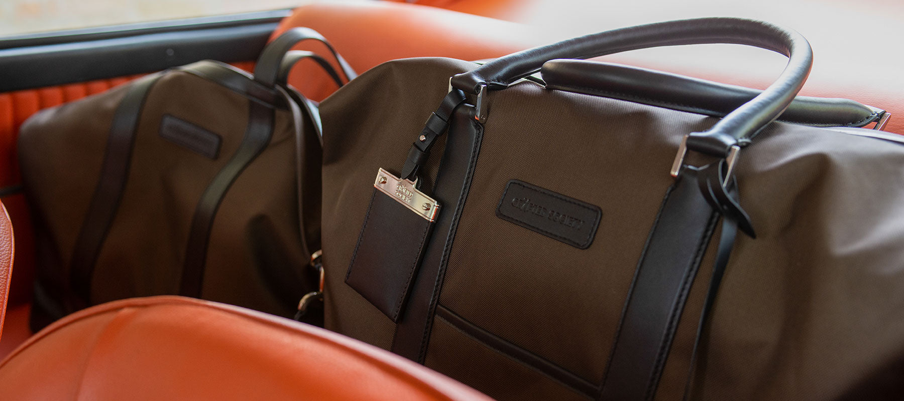 weekender bags in chocolate econyl and black nappa leather on backseat of a vintage car