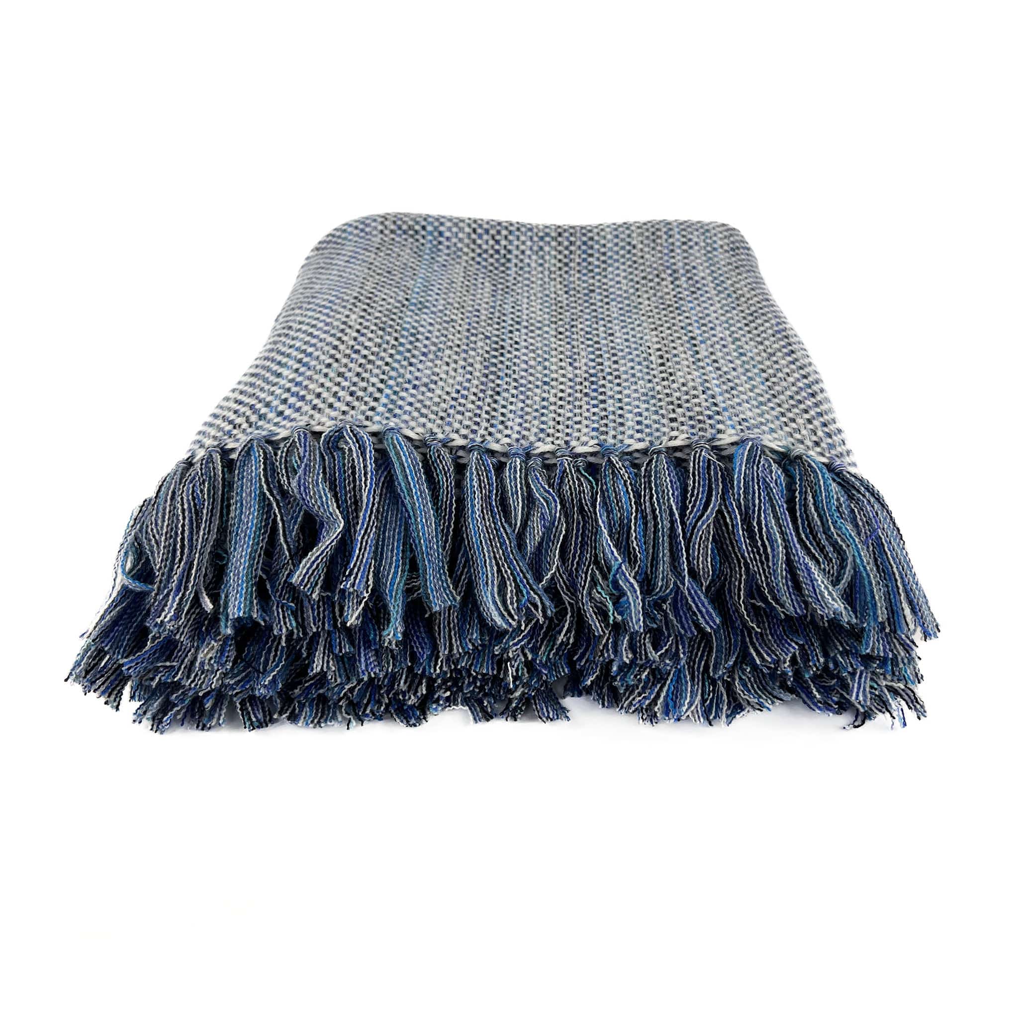 An Italian made Cashmere throw with a white weft and different shades of blue warp, folded on a white background with handknotted multiple shades of blue tassels showing in front