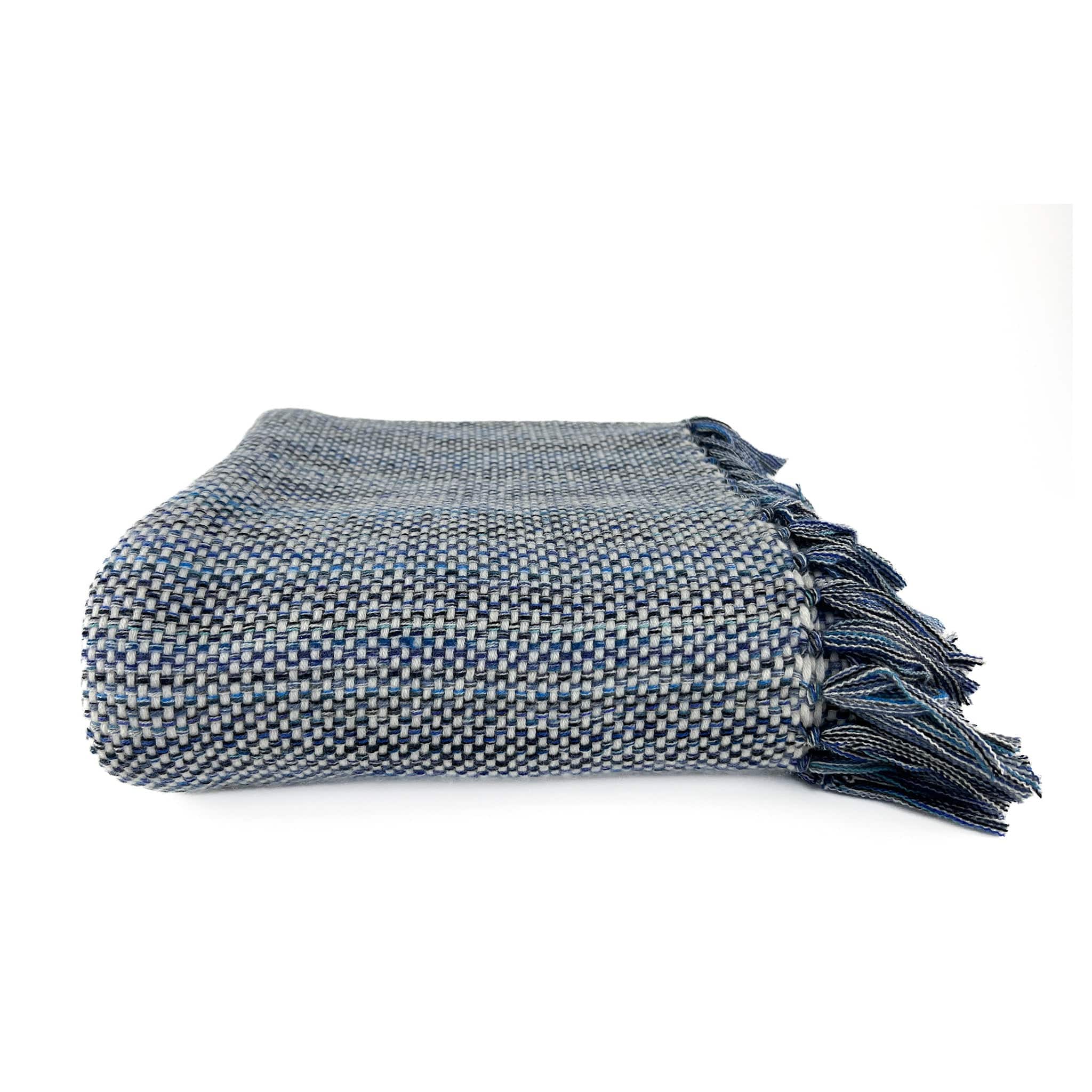 An Italian made Cashmere throw with a white weft and different shades of blue warp, folded on a white background with handknotted multiple shades of blue tassels showing on the right hand side