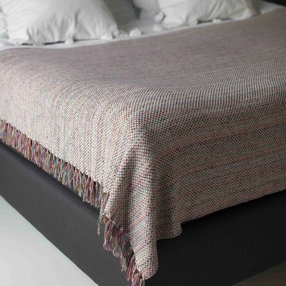Italian made cashmere throw in multicolour, draped over a dark grey bed with the throws tassels visible on the left side