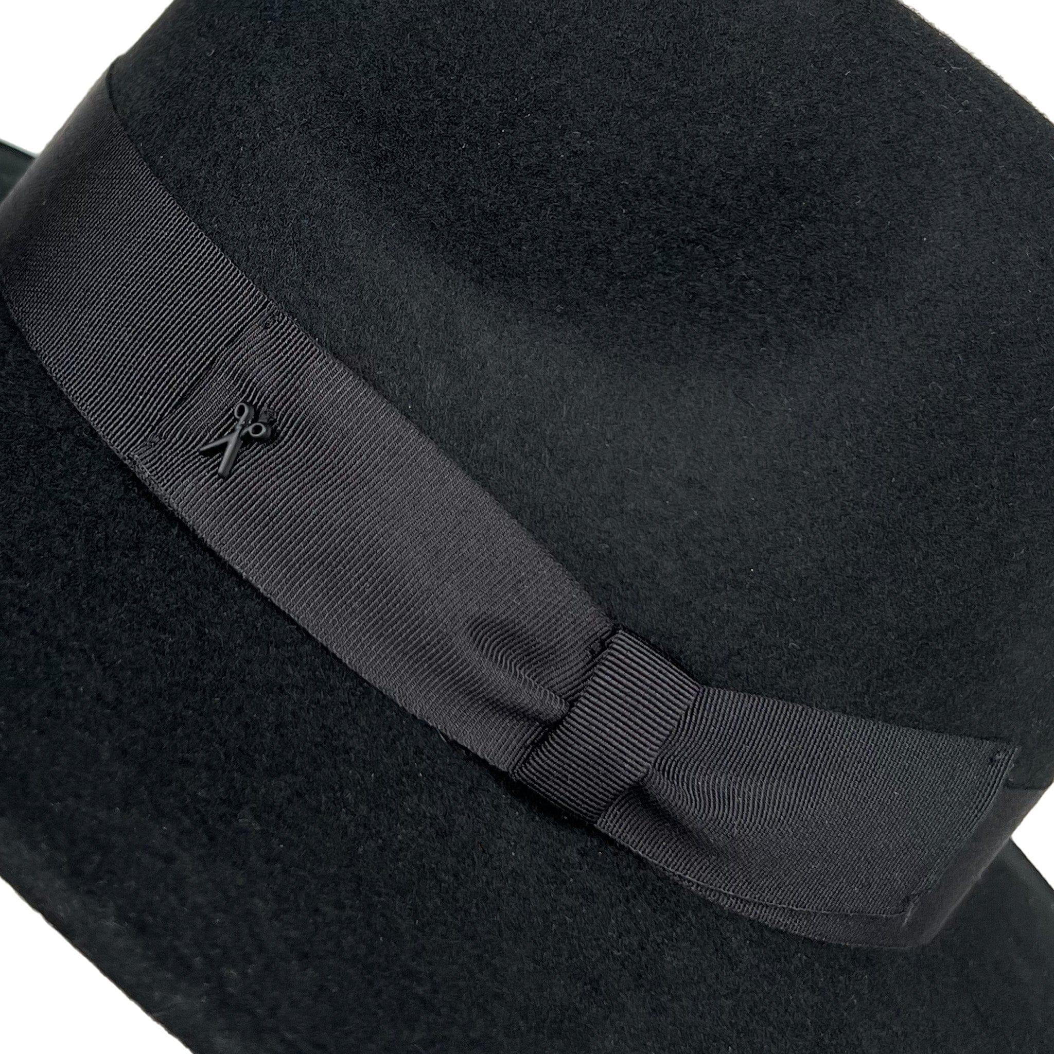 Virgin wool light felt fedora hat in black with black gross grain ribbon and bow, with iconic black crafted society scissor on the left side. 100% virgin wool, water repellent and crushable. zoomed in detail of bow and scissor